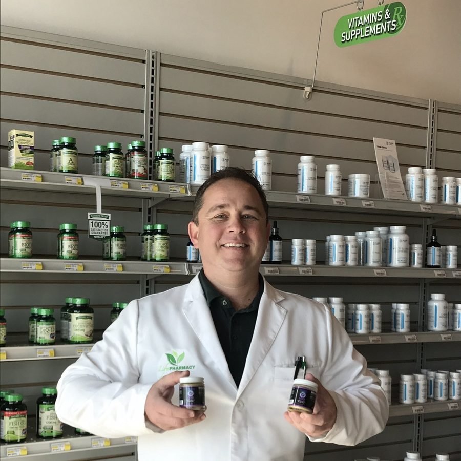 A pharmacist holding two products in front of the supplement shelves